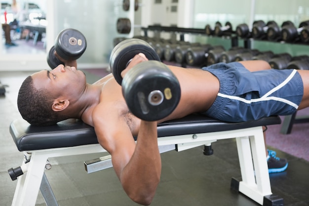 Vista laterale dell&#39;uomo senza camicia che si esercita con i dumbbells in ginnastica