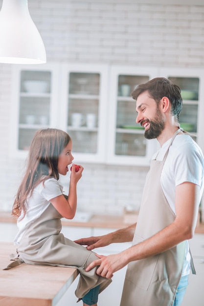 Vista laterale della bambina che mangia pomodoro ciliegino con il padre sulla cucina domestica