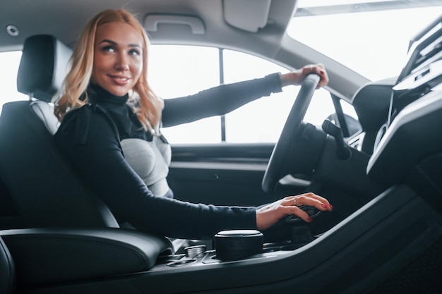 Vista laterale della bella bionda in abiti eleganti che si siede all'interno di un'auto moderna