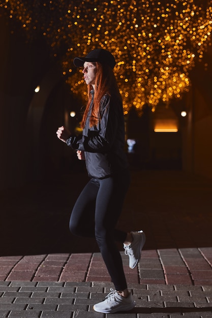Vista laterale della donna atleta vestita di nero che corre di notte jogger femminile che si esercita all'a...