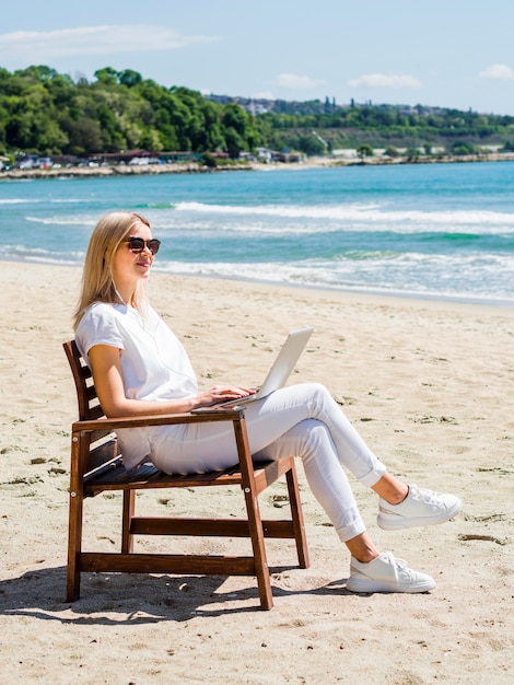 Vista laterale della donna che lavora al computer portatile in spiaggia