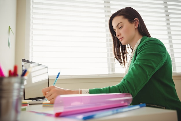 Vista laterale della donna che scrive mentre è seduto al tavolo