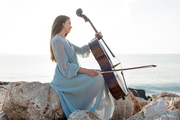 Vista laterale della donna che suona il violoncello sulle rocce in riva al mare