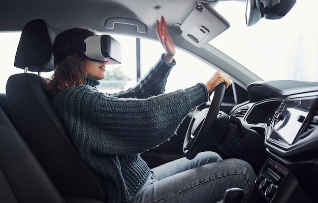 Vista laterale della donna con gli occhiali per realtà virtuale che si trovano all'interno di un'auto moderna.