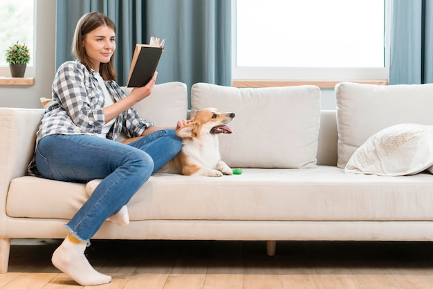 Vista laterale della donna con il cane che legge un libro sul divano