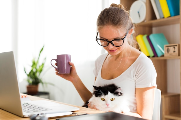 Vista laterale della donna con il gatto allo scrittorio che lavora dalla casa