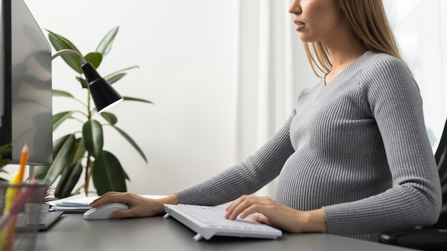 Vista laterale della donna d'affari incinta alla sua scrivania in ufficio