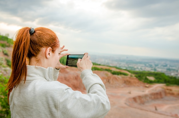 Vista laterale della donna dello zenzero che fa foto sullo smartphone