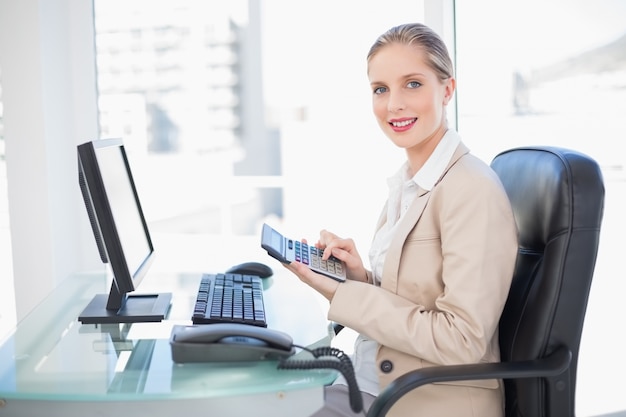 Vista laterale della donna di affari bionda sorridente che per mezzo del calcolatore