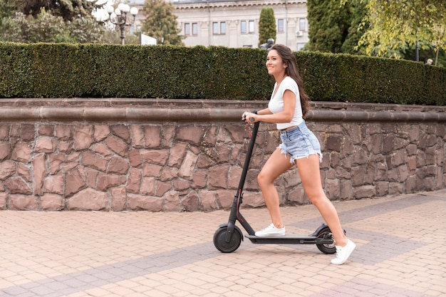 Vista laterale della donna sorridente in sella a uno scooter in città