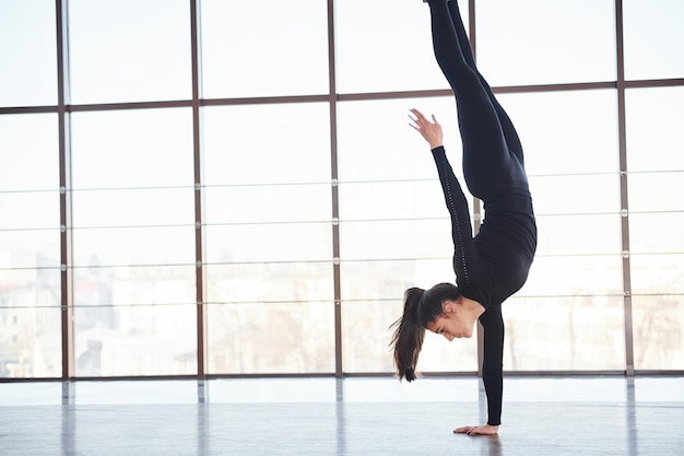 Vista laterale della donna sportiva in abbigliamento sportivo che fa acrobazie atletiche contro la finestra.