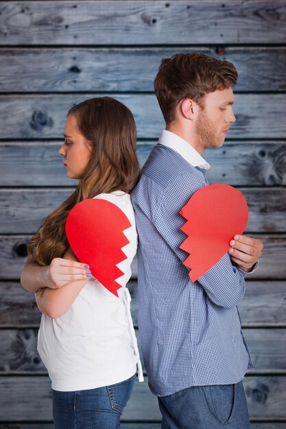 Vista laterale della giovane coppia che tiene il cuore spezzato su sfondo di legno in blu