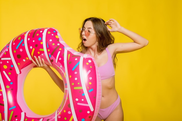 Vista laterale della giovane donna attraente in occhiali da sole alla moda da bagno che tengono l'anello di nuotata a forma di ciambella