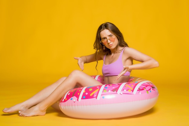 Vista laterale della giovane donna attraente in occhiali da sole alla moda da bagno che tengono l'anello di nuotata a forma di ciambella