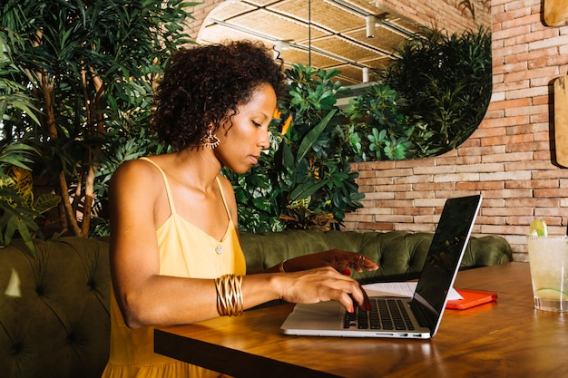 Vista laterale della giovane donna che utilizza computer portatile sulla tavola di legno nel ristorante