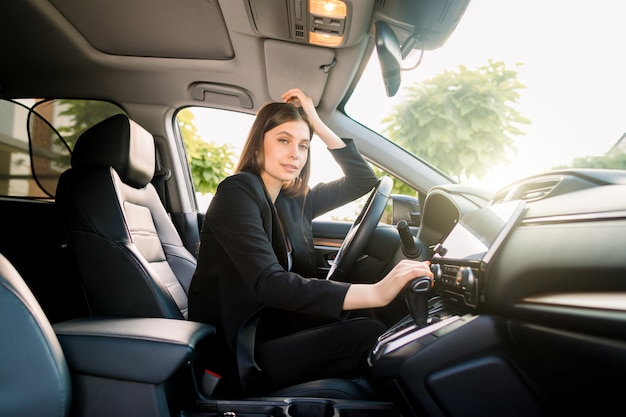 Vista laterale della giovane e bella donna d'affari seduto nella sua auto sul sedile di guida Giornata di sole. Donna d'affari in auto