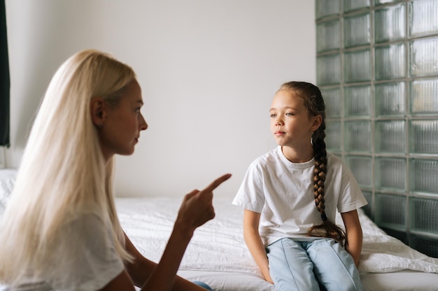 Vista laterale della giovane madre arrabbiata che rimprovera alzando la voce urlando e gesticolando con le mani alla figlia ostinata e difficile a casa