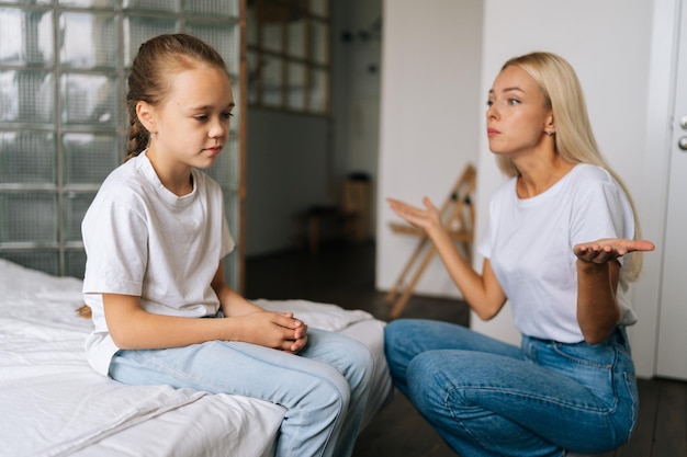 Vista laterale della giovane madre irritata che rimprovera alzando la voce urlando e gesticolando con le mani alla figlia ostinata e difficile a casa