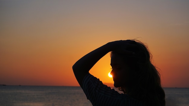 Vista laterale della luce posteriore di una silhouette di donna caldo tramonto davanti al sole - spiaggia turistica al tramonto