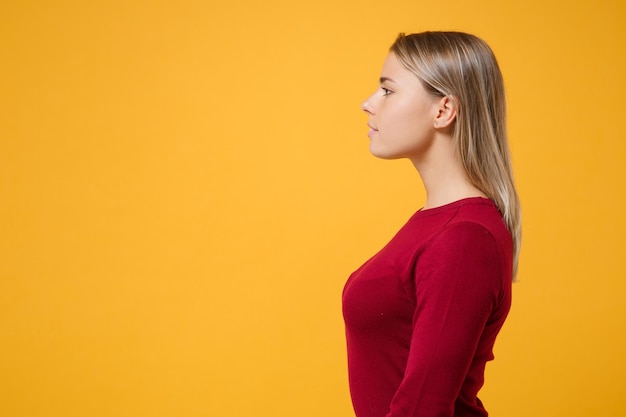 Vista laterale della ragazza bella giovane donna bionda in abiti casual in posa isolata sul ritratto in studio di sfondo parete giallo arancio. Concetto di stile di vita di emozioni della gente. Simula lo spazio della copia. Guardando da parte.