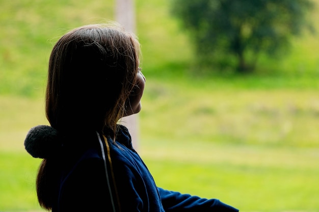 Vista laterale della ragazza che guarda fuori dalla finestra a pioggia