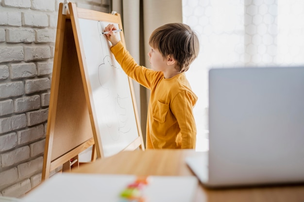 Vista laterale della scrittura del bambino a casa sulla lavagna mentre istruito online