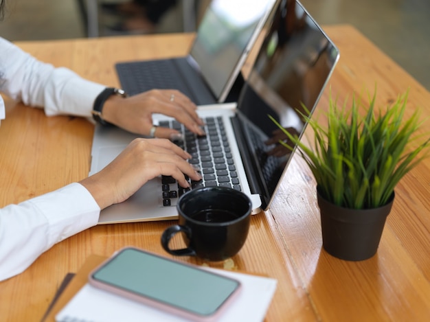 Vista laterale delle mani femminili che lavorano con laptop, tablet, smartphone e scartoffie sulla scrivania in legno