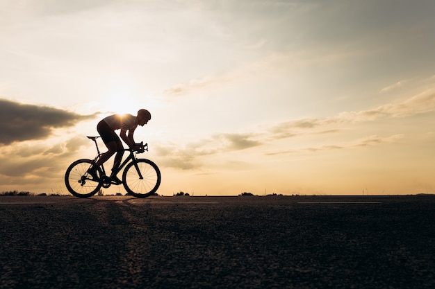 Vista laterale dello sportivo attivo nel casco protettivo in sella a bici tra la natura durante il tramonto