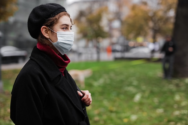 Vista laterale di affascinante giovane donna che cammina per strada e indossa una maschera medica durante l'epidemia di coronavirus. Concetto di protezione e prevenzione.