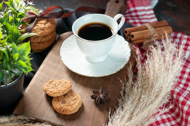 Vista laterale di deliziosi biscotti impilati legati con nastro su tavola di legno e tazza di caffè su tavola di legno punte asciugamani fiore cannella lime su sfondo scuro colori misti