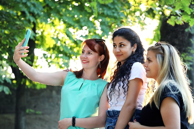 Vista laterale di tre giovani donne sorridenti fanno selfie nel parco