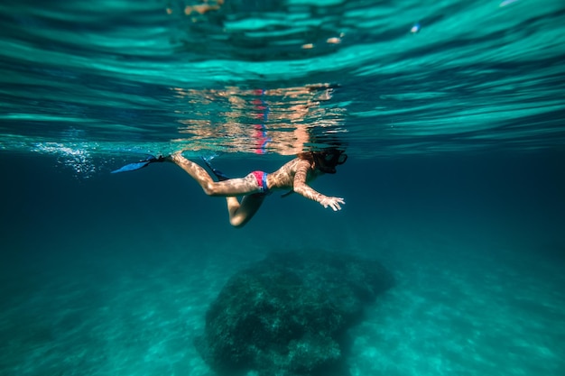 Vista laterale di un adolescente anonimo che galleggia nell'acqua marina blu profondo con le pinne e la maschera da snorkeling