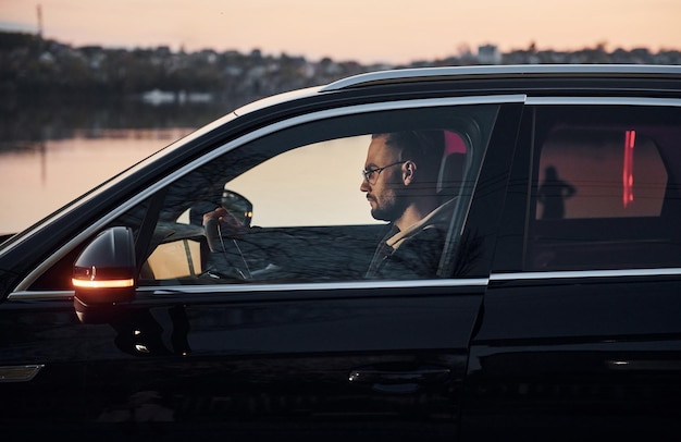 Vista laterale di un bell'uomo con la barba lunga in abiti alla moda che guida la sua automobile