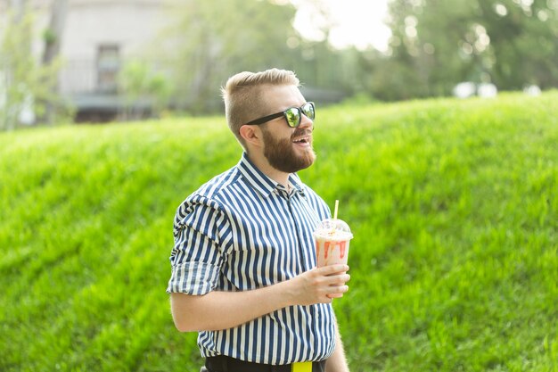 Vista laterale di un giovane alla moda con la barba che tiene un frappè e ammira la vista sulla città