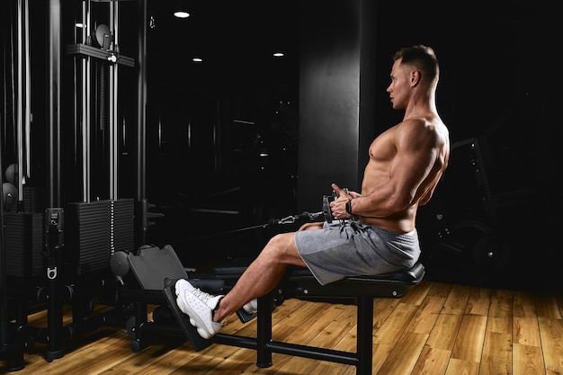 Vista laterale di un giovane forte con corpo atletico facendo esercizi su attrezzature per il fitness in una palestra scura.