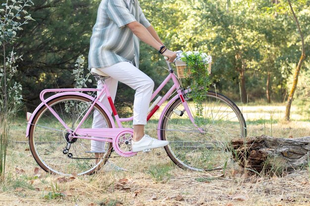 Vista laterale di un giovane hipster irriconoscibile su una bici vintage rosa con ambiente naturale