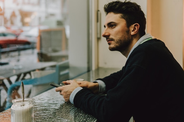 Vista laterale di un giovane uomo d'affari seduto accanto alla finestra di un caffè