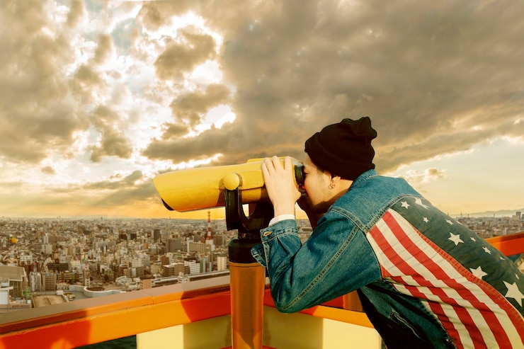 Foto vista laterale di un uomo che guarda attraverso un binocolo a moneta in città contro un cielo nuvoloso durante il tramonto