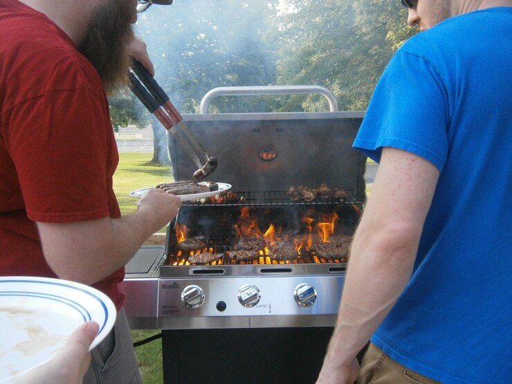 Foto vista laterale di un uomo che serve salsicce a un amico bruciando un barbecue