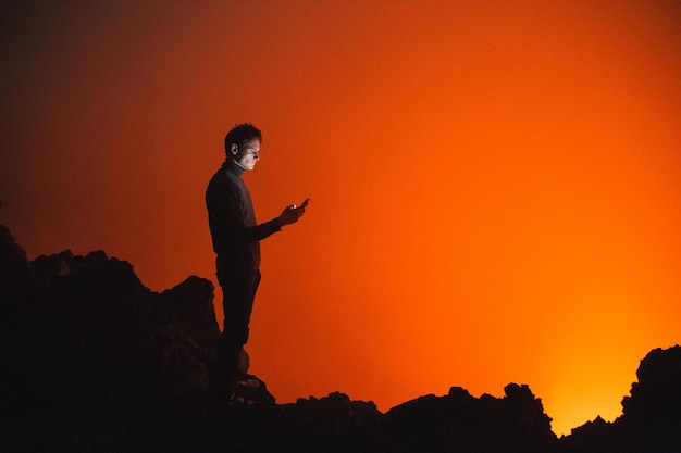 Vista laterale di un uomo che usa un telefono cellulare mentre si trova su rocce di silhouette durante il tramonto