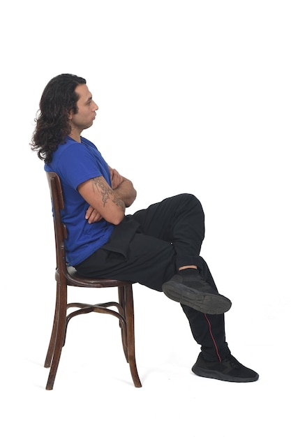 Vista laterale di un uomo con abbigliamento sportivo seduto su gambe di sedia e braccia incrociate su sfondo bianco