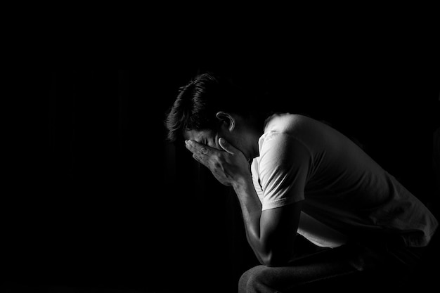 Vista laterale di un uomo depresso con la testa tra le mani su uno sfondo nero.