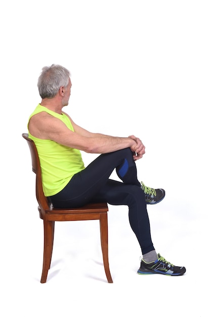 Vista laterale di un uomo in calzamaglia sportiva e senza maniche giallo fluorescente seduto su una sedia che guarda lo sfondo e le gambe incrociate su sfondo bianco