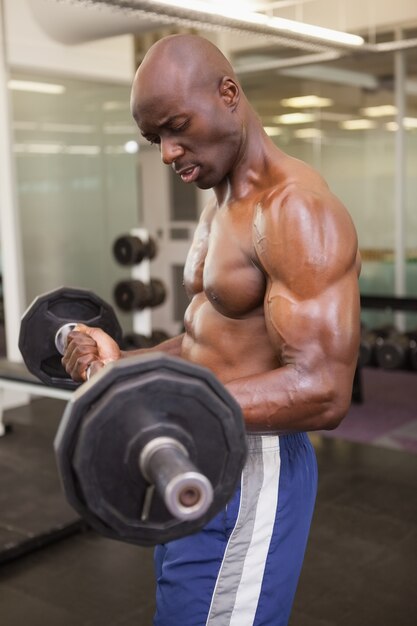 Vista laterale di un uomo muscolare senza camicia che solleva bilanciere in palestra