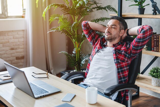 Vista laterale di un uomo sorridente e calmo felice che riposa dopo aver risolto i compiti sul posto di lavoro dell'ufficio a casa