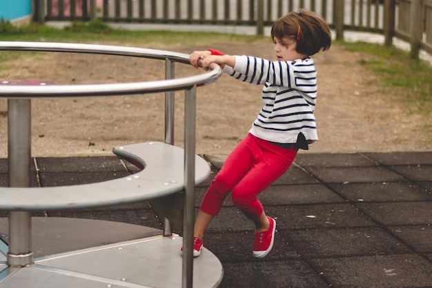 Vista laterale di una bambina che spinge una giostra rotante in un parco giochi