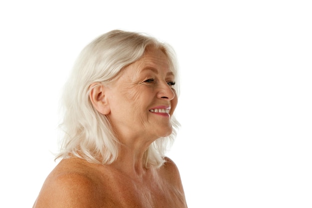 Vista laterale di una bella donna senior con i capelli biondi in piedi che sorride contro lo studio bianco