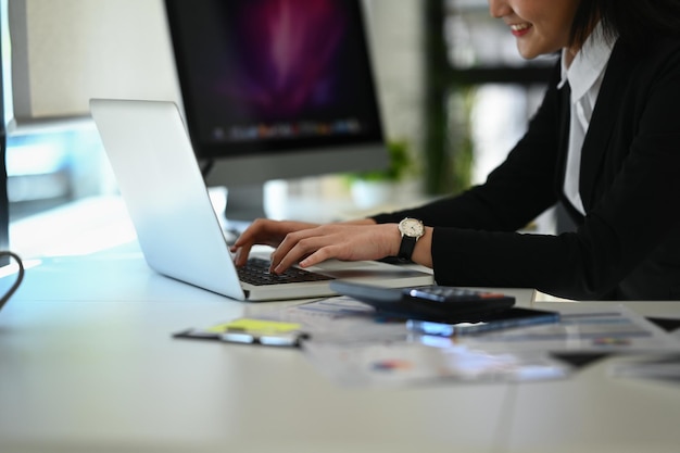 Vista laterale di una contabile sorridente in abito nero che utilizza un laptop per controllare le informazioni online