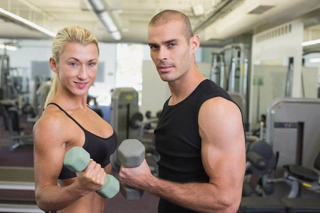 Vista laterale di una coppia che si esercita con i dumbbells in ginnastica