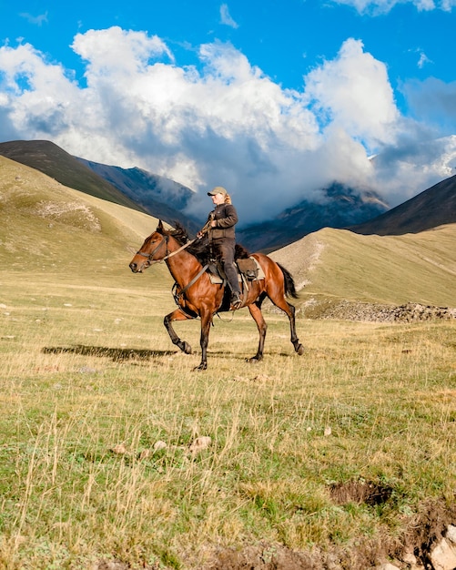 Vista laterale di una cowgirl pastore a cavallo su una valle di montagna contro il cielo con le nuvole